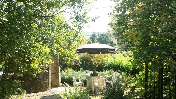 Un patio jardín con mesa y sillas, rodeado de vegetación exuberante y un muro de piedra.