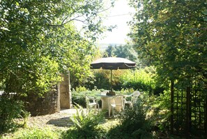 Ein Garten-Terrasse mit Tisch und Stühlen, umgeben von üppigem Grün und einer Steinmauer.