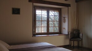 Un dormitorio con un ventanal grande, una cama con colcha, una silla y un móvil colgante.