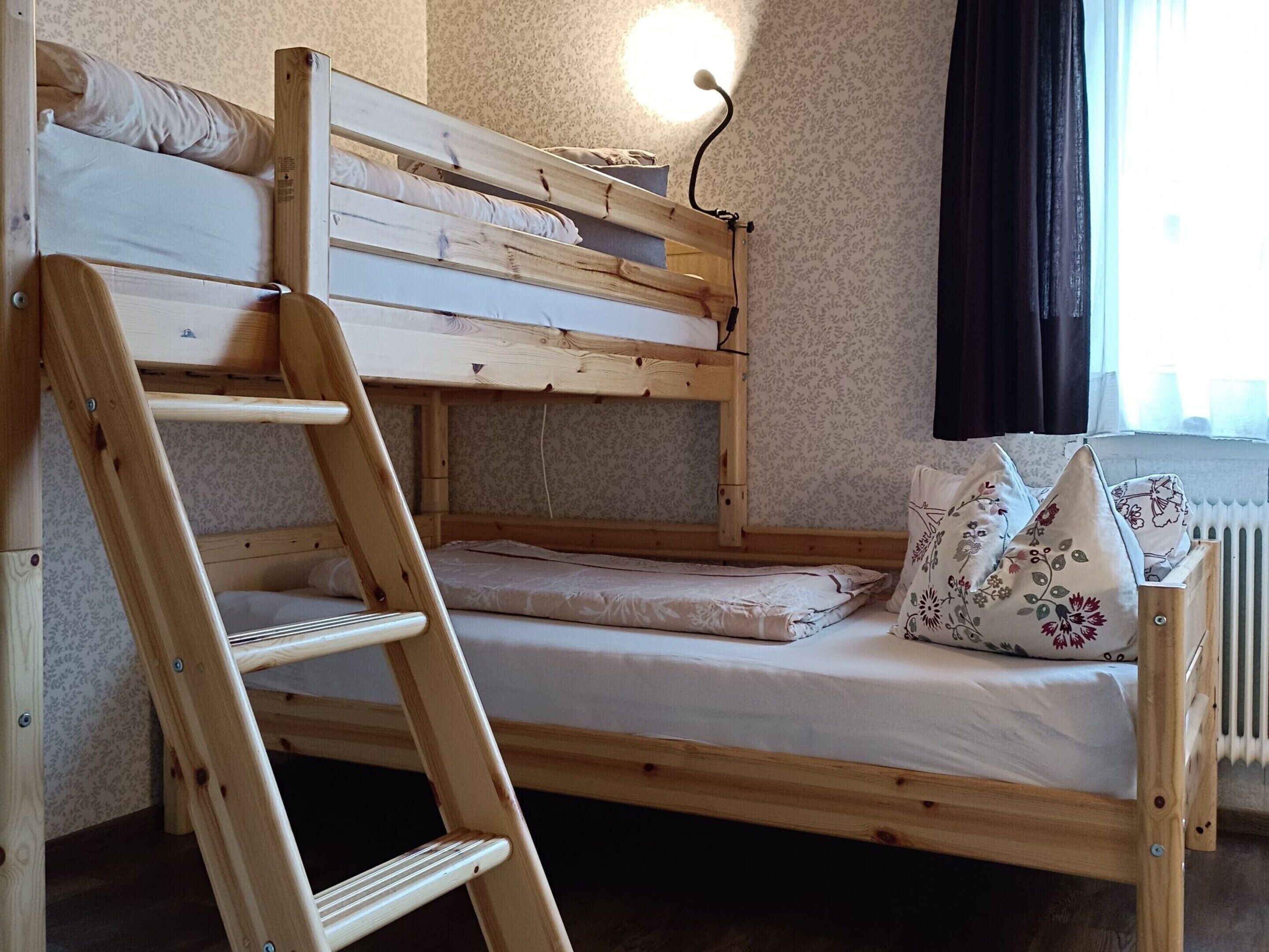 A bunk bed with a wooden ladder, a bedside table, and a nightstand.