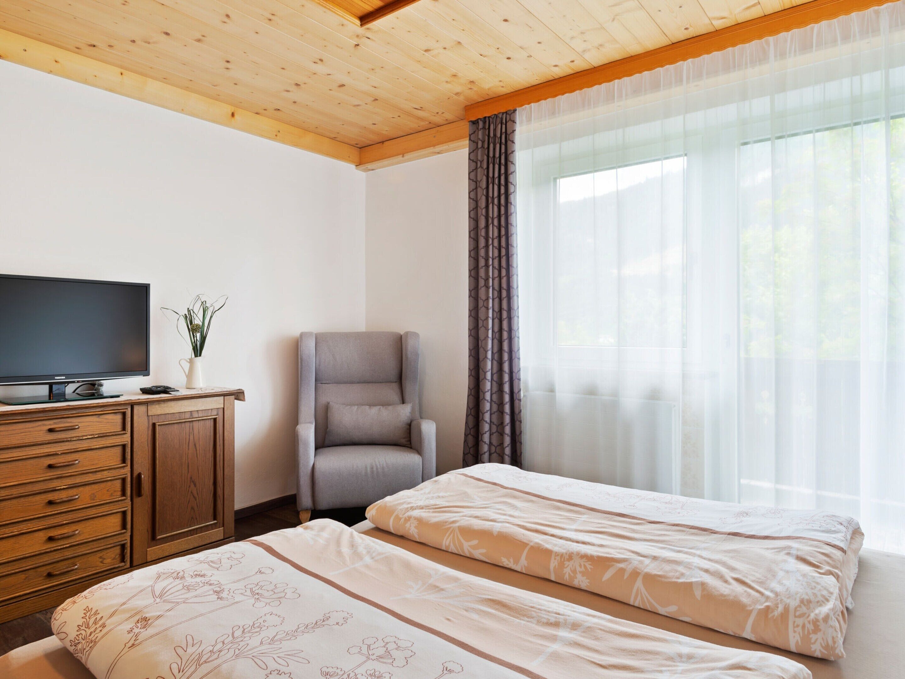 A bedroom with two beds, a TV, a chair, and a wooden dresser.