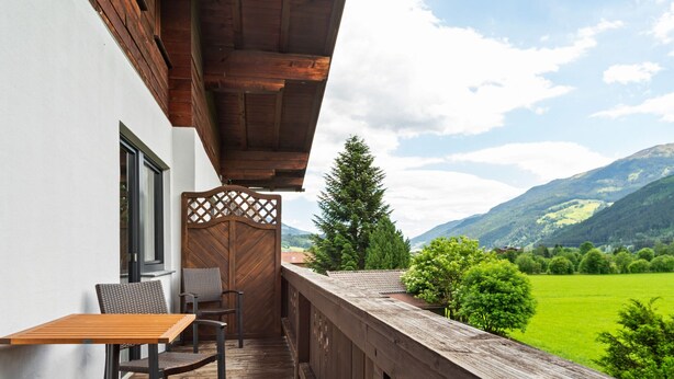 A wooden deck with a table and chairs, overlooking a green landscape and mountains. - Cosy Apartment in Muhlbach With Balcony (Bramberg am Wildkogel)