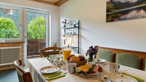 A dining area with a table set for breakfast, a radiator, a window with a view of greenery, and a metal shelf with decorative items. - Cosy Apartment in Muhlbach With Balcony (Bramberg am Wildkogel)