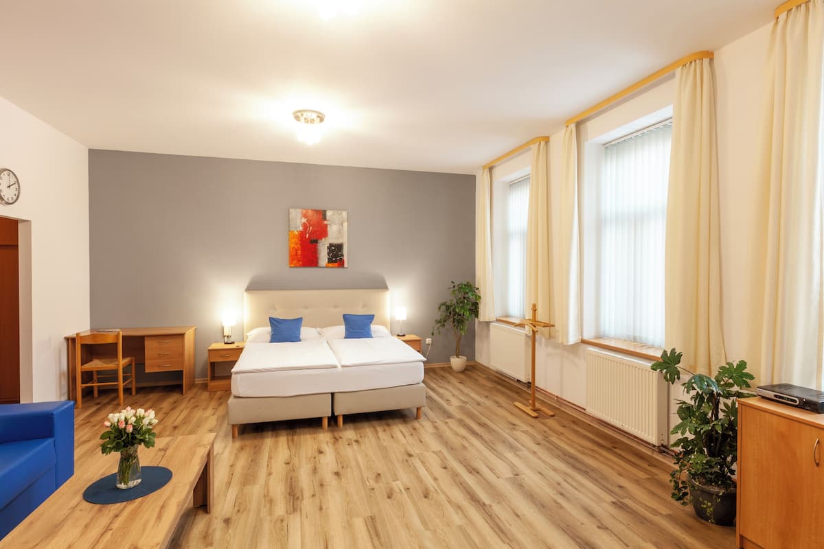 A bedroom with a bed, bedside tables, a desk, a chair, a potted plant, and a window with curtains.