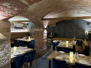Restaurante com paredes de pedra, mesas de madeira e cadeiras azuis.