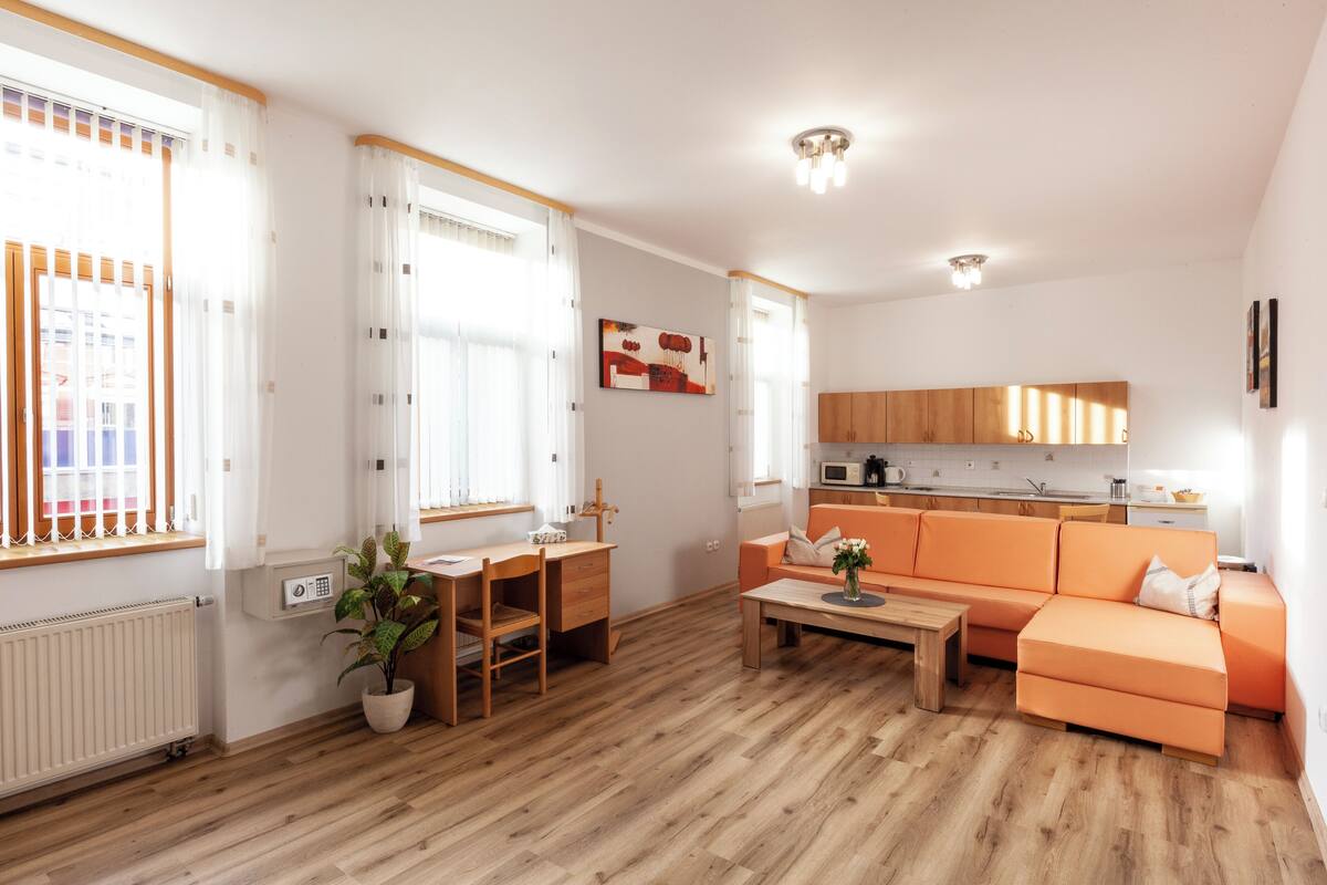 A modern living room with a wooden floor, a sofa, a dining table, and a kitchen area with cabinets and a microwave.