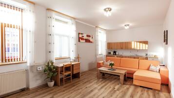 Uma sala de estar moderna com piso de madeira, um sofá, uma mesa de jantar e uma área de cozinha com armários e micro-ondas.