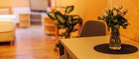 Una sala de estar con una mesa de comedor, un florero con flores y un televisor al fondo.