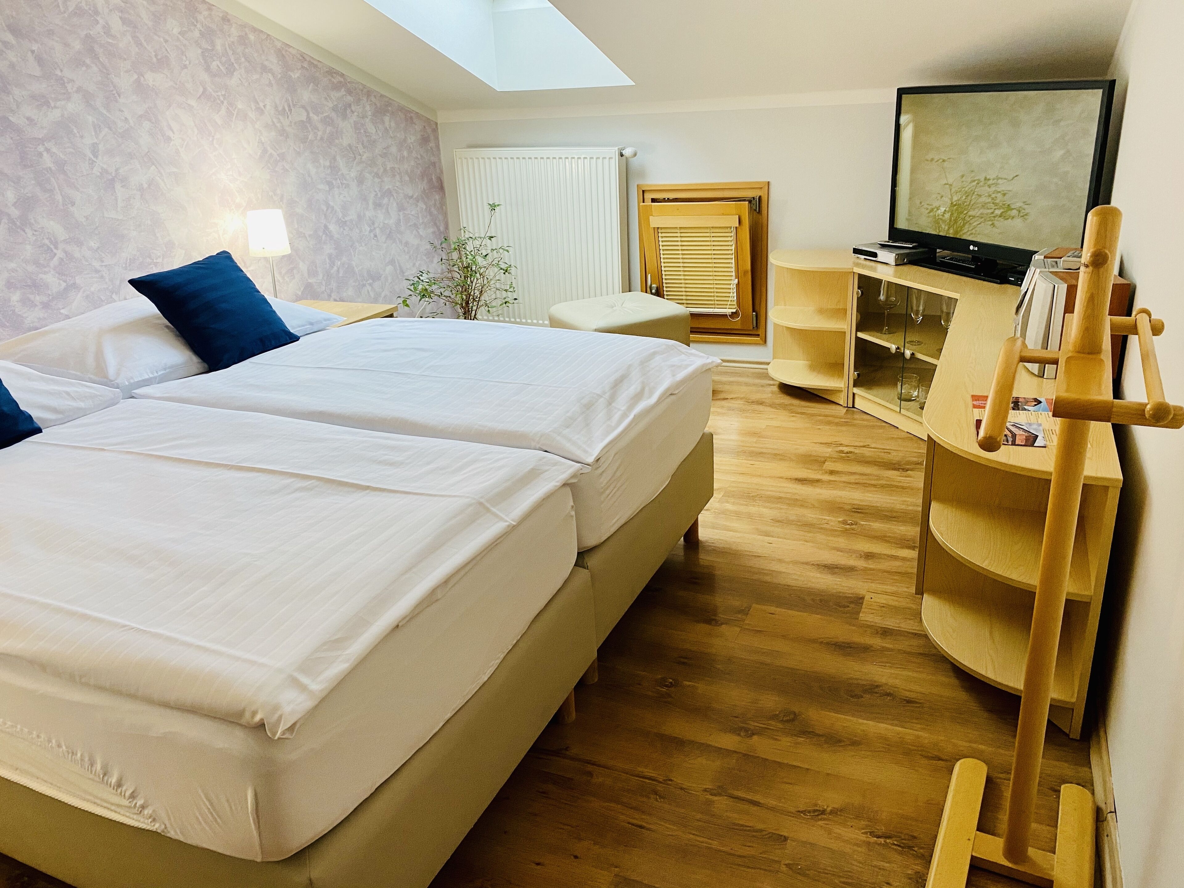 Una habitación de hotel con dos camas, televisión, aparador de madera y tragaluz.
