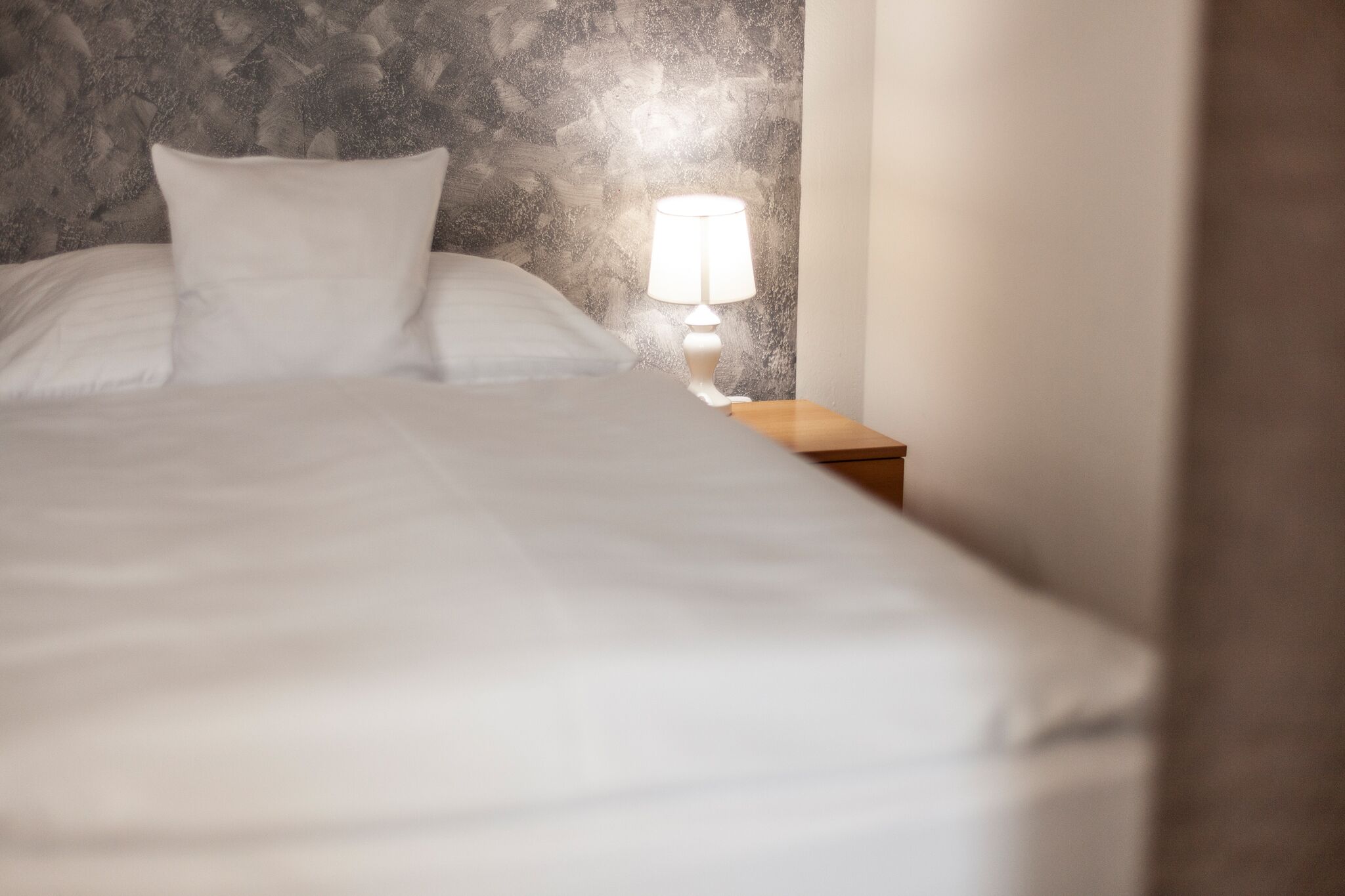 Una cama con ropa de cama blanca y una mesita de noche con lámpara.