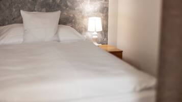 Un letto con lenzuola bianche e un comodino con una lampada.