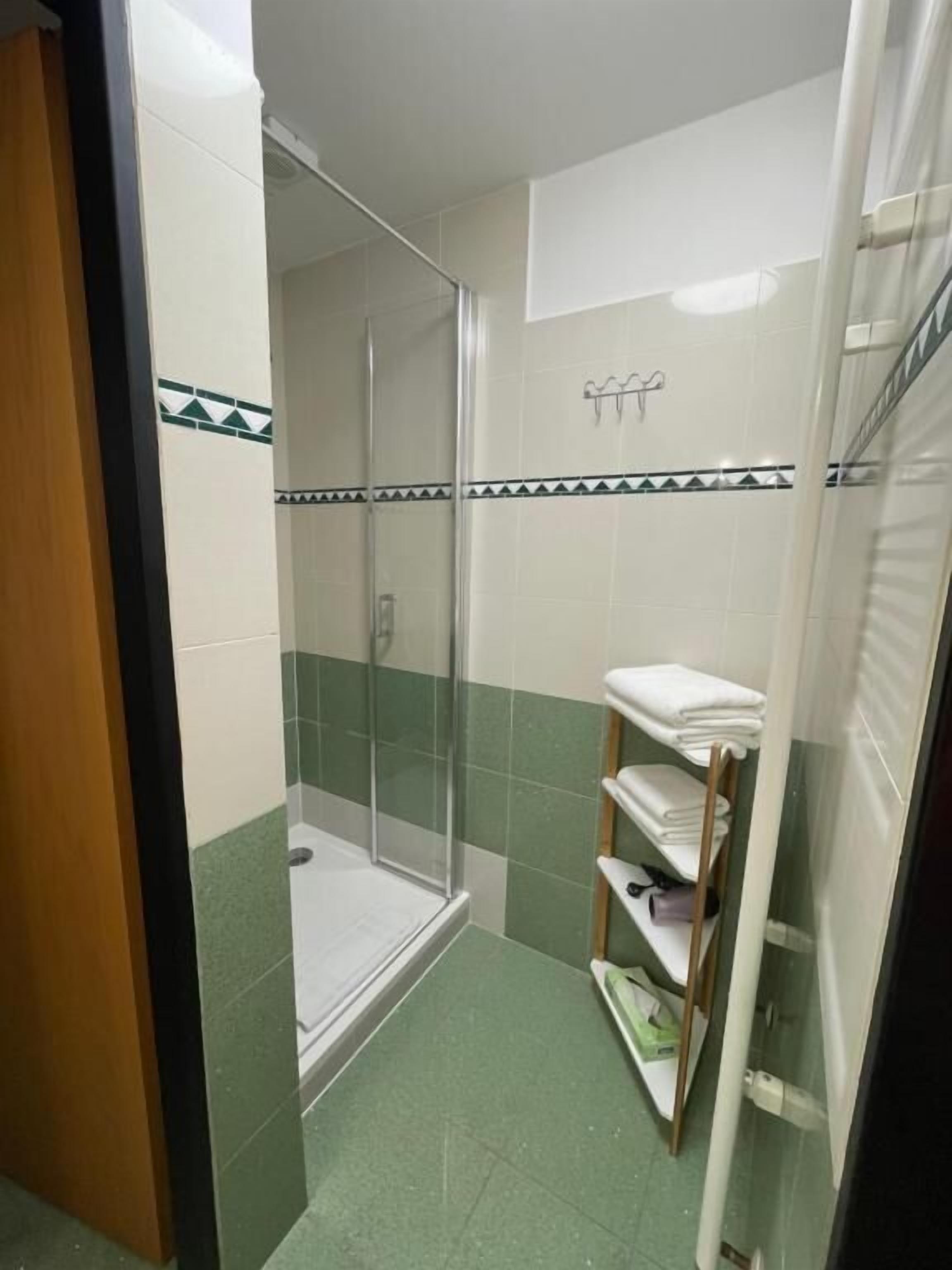 Une salle de bain avec une douche à parois de verre, un carrelage au sol et une étagère avec des serviettes.