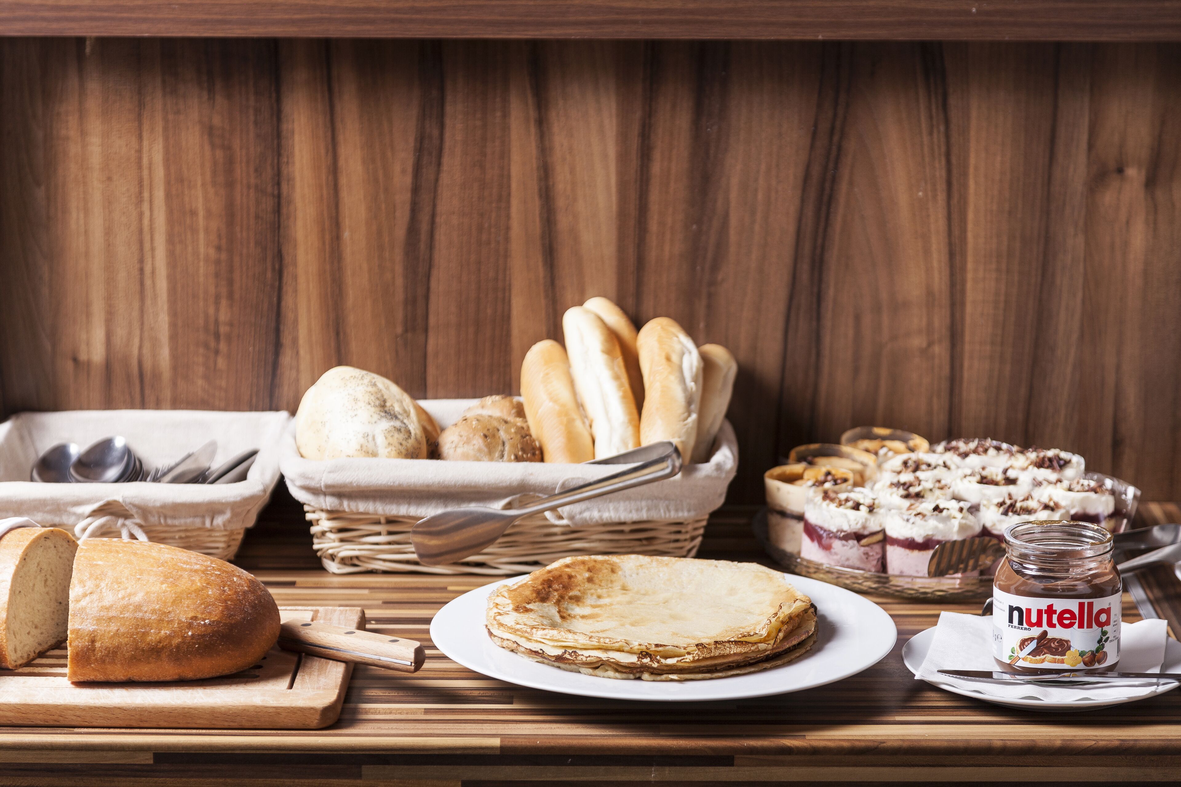 A wooden table with a variety of breads, a pie, and a Nutella jar.
