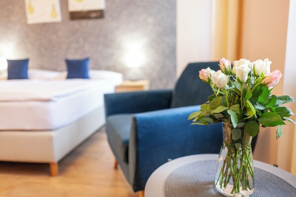 A hotel room with a bed, a chair, a vase with flowers, and a bedside table. - Penzion Pohoda (Trutnov)