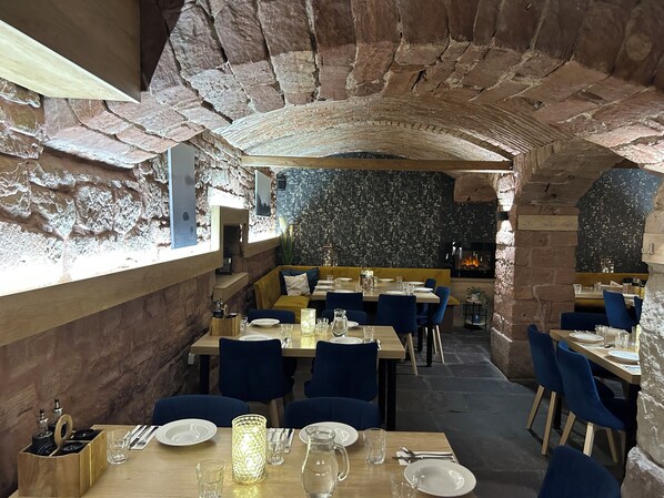 A restaurant with stone walls, wooden tables, and blue chairs.