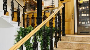 A staircase with ornate black railings, a wooden handrail, and a glass cabinet with bottles. - Penzion Pohoda (Trutnov)