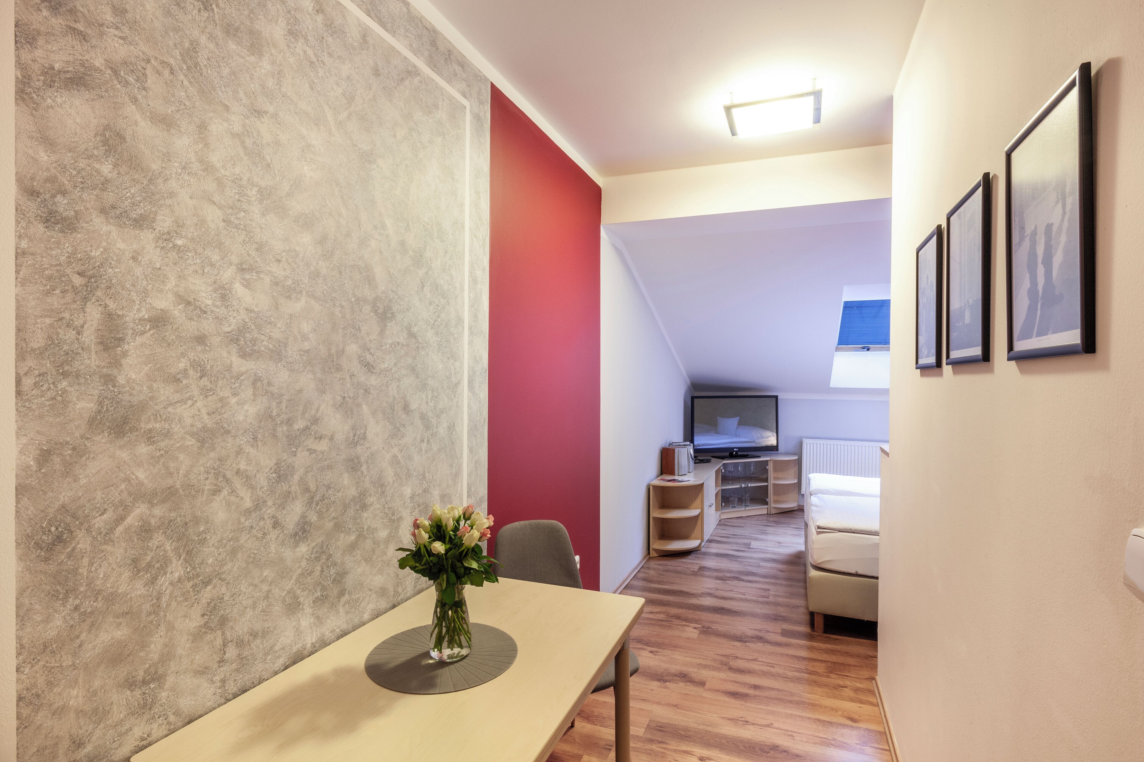 A modern room with a dining table, a red accent wall, a TV, and a sofa.