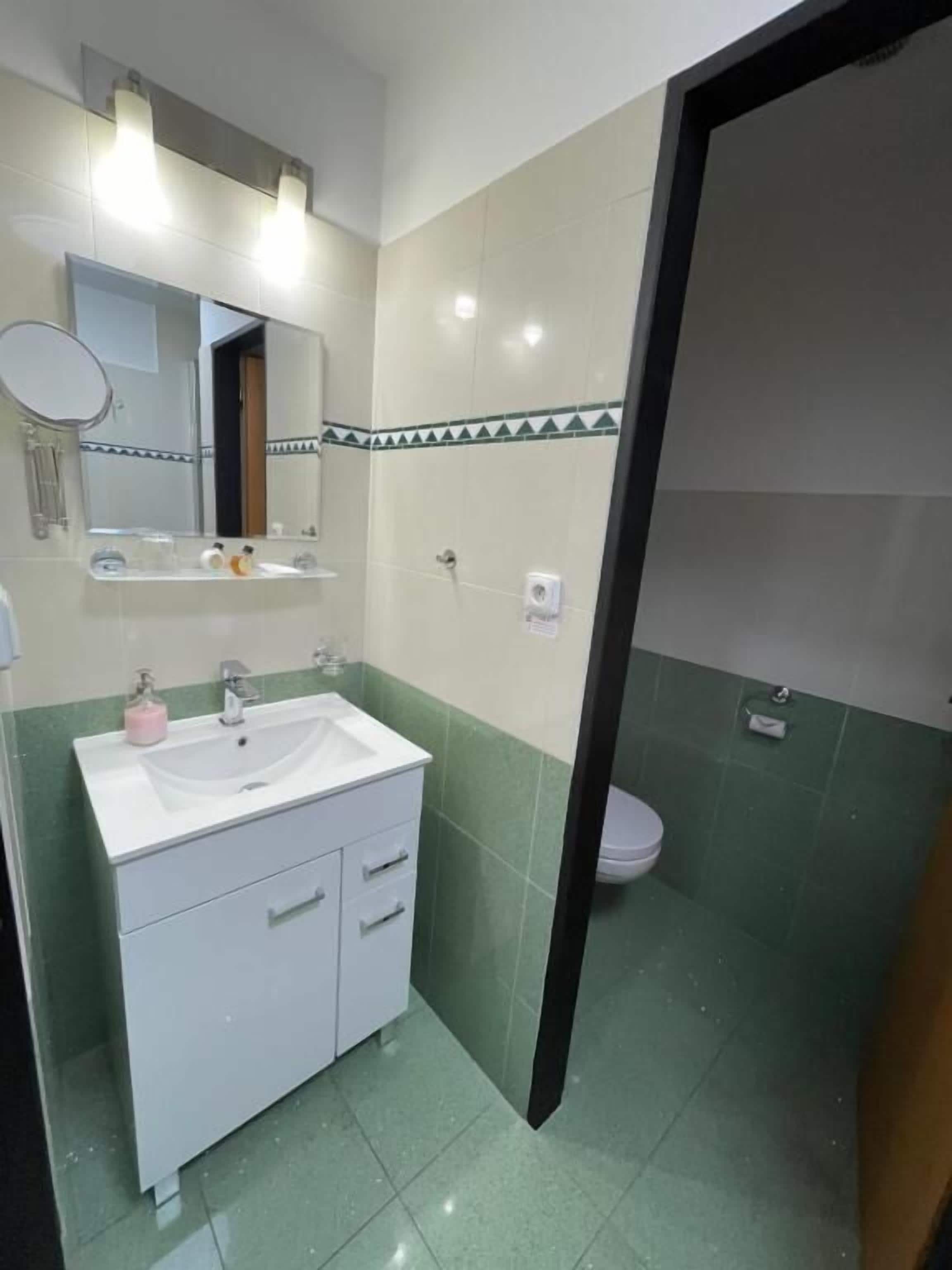 A bathroom with a white sink, mirror, and green-tiled walls.