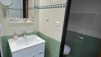 A bathroom with a white sink, mirror, and green-tiled walls.