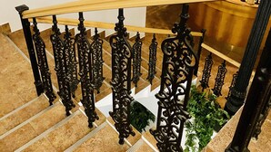 Una escalera con barandillas negras ornamentadas y un pasamanos de madera que lleva a un rellano con diplomas enmarcados en la pared.