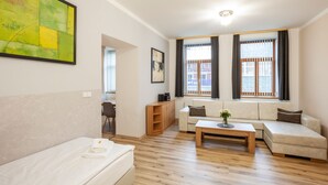 A modern living room with a sofa, a coffee table, and a dining table. There are two windows with curtains, a painting on the wall, and a small cabinet. - Penzion Pohoda (Trutnov)