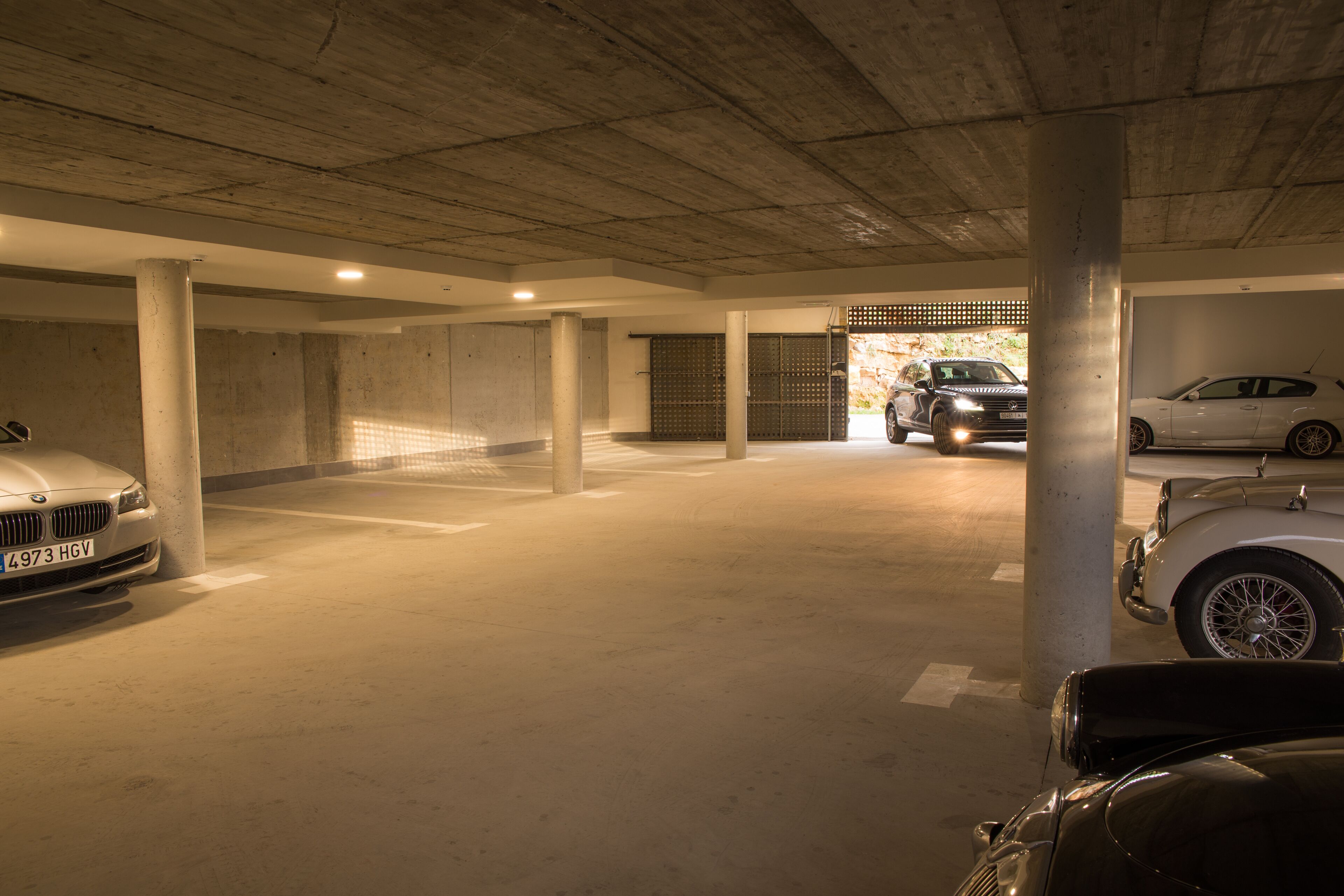 Un garaje para estacionar con pilares de concreto, un auto blanco y un auto clásico.