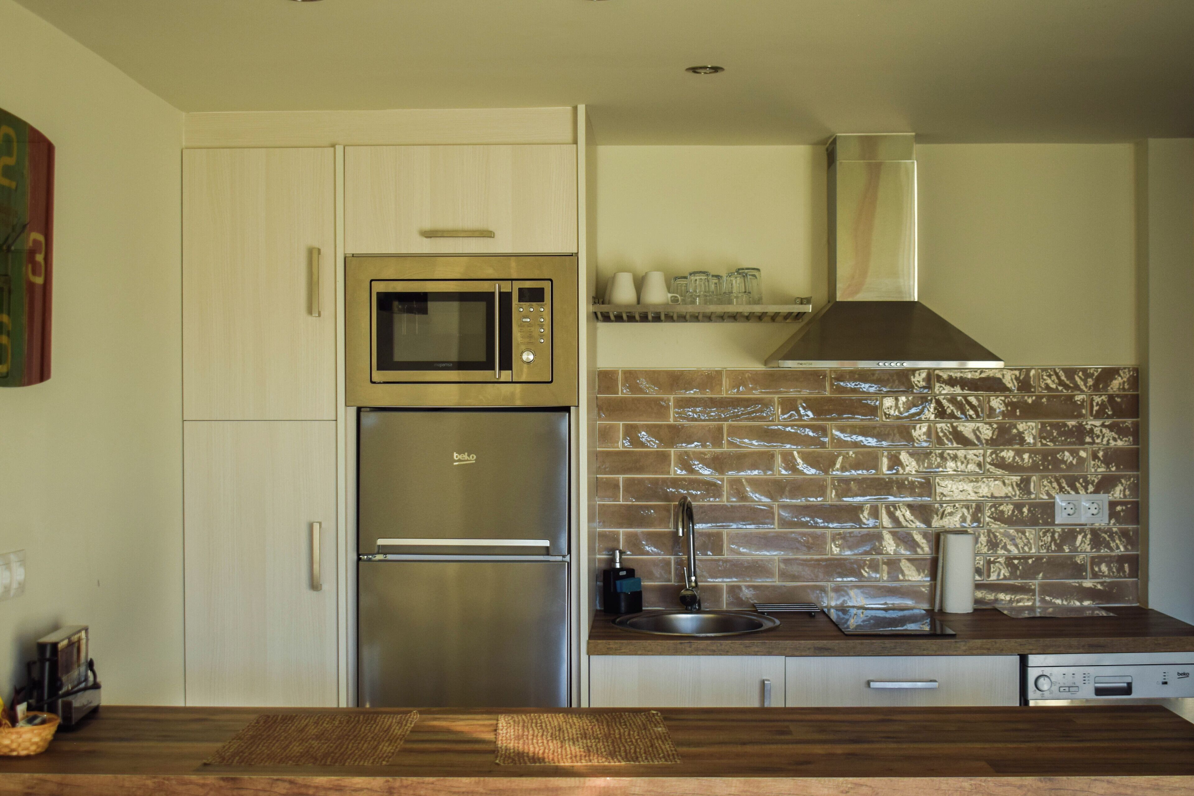 A modern kitchen with stainless steel appliances, a wooden countertop, and a brick backsplash.