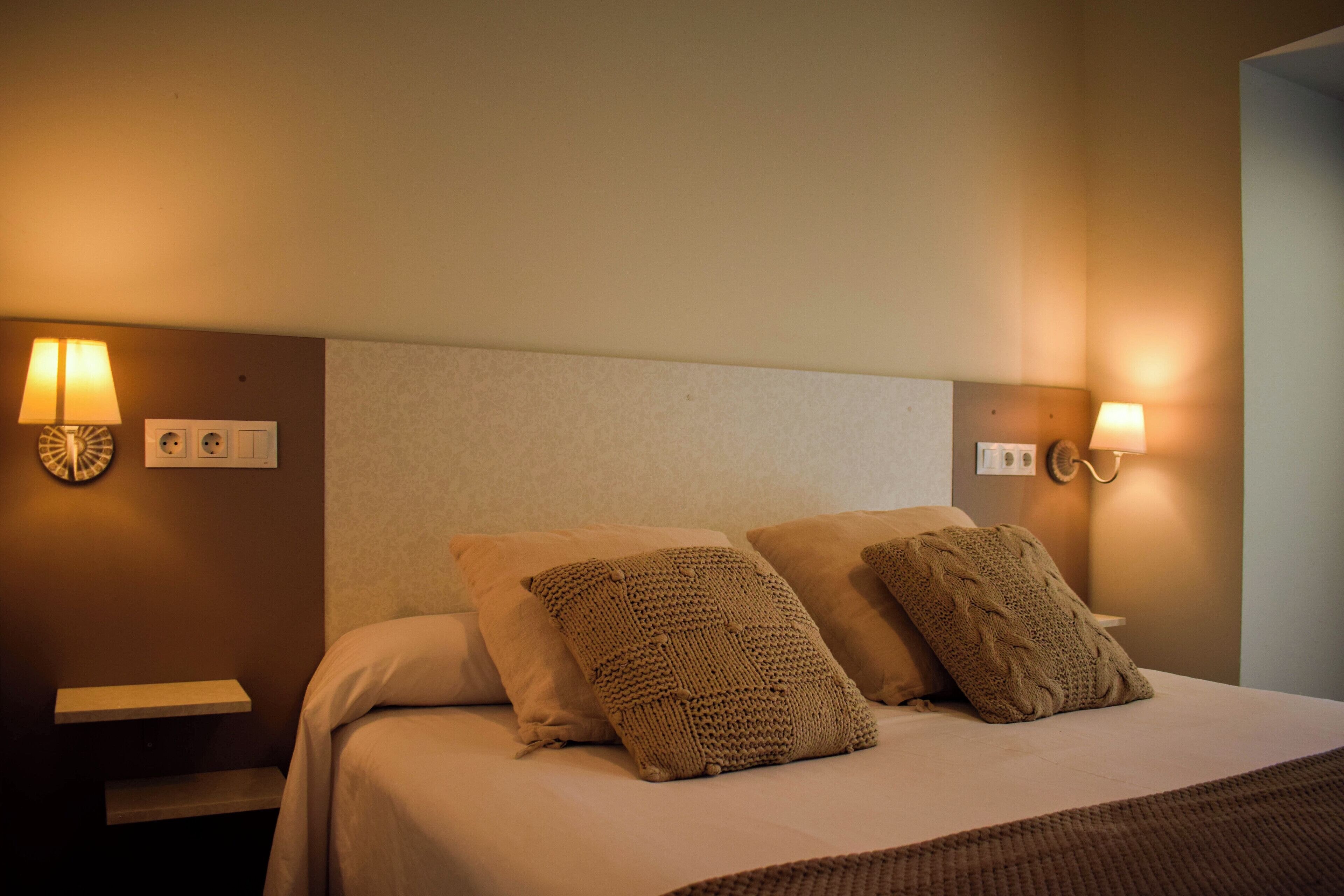 A neatly made bed with two pillows and a blanket, bedside lamps, and a small shelf on the nightstand.
