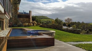 Ein Poolbereich mit Whirlpool, Steinmauern und Blick auf eine grüne Landschaft.