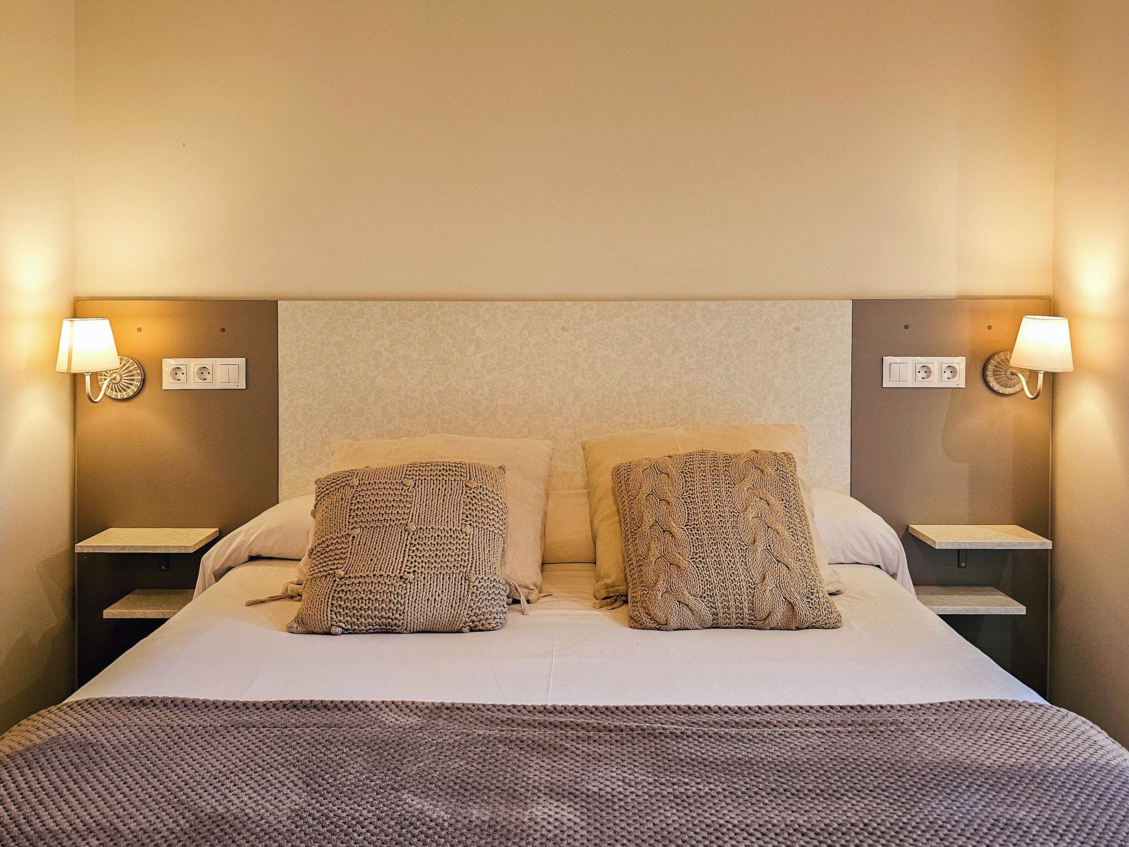 Een hotelkamer met een groot bed, twee nachtkastjes, twee wandlampen en een gestructureerd hoofdeinde.