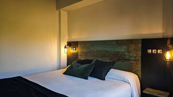 Un dormitorio moderno con una cama grande, dos lámparas de lectura fijadas a la pared y una pared rústica con textura detrás de la cama.