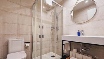 A modern bathroom with a glass-enclosed shower, a white toilet, a sink with a mirror, and a towel rack.
