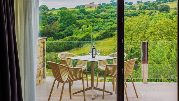 Ein Balkon mit Tisch und Stühlen, mit Blick auf eine üppige, grüne Landschaft.