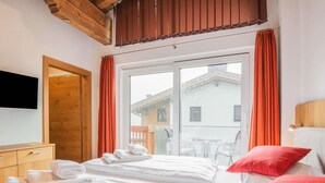 Una camera d'albergo con un letto, una cassettiera in legno, una TV a parete e un balcone con tende arancioni.