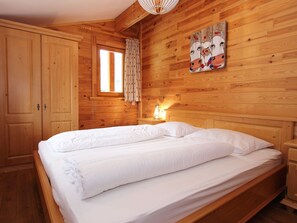 Una habitación de madera con cama, mesita de noche, ventana con cortinas y un cuadro en la pared.