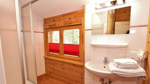 A bathroom with a shower, wooden paneling, a window with red blinds, a sink with a mirror, and towels stacked on a rack. - Comfortable Chalet With Whirlpool and Sauna in Krimml (Krimml)