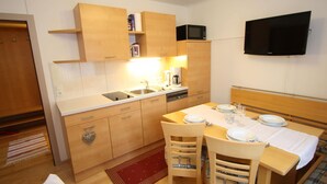 A compact kitchen with wooden cabinets, a microwave, and a coffee maker. There is a dining table set with plates and glasses. - Apartment in Niedernsill Near Zell am See Ski Area (Niedernsill)