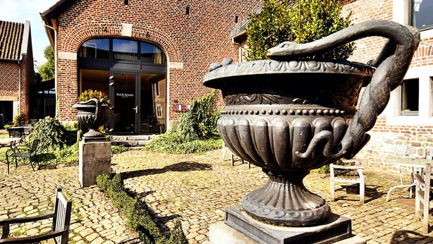 A courtyard with a large urn sculpture, brick buildings, and outdoor seating. - Pleasing Holiday Home in Richelle With Garden, Terrace, BBQ (Vise)