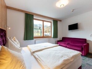 Een kamer met een bed, een raam met gordijnen, een flatscreen televisie en een paarse bank.