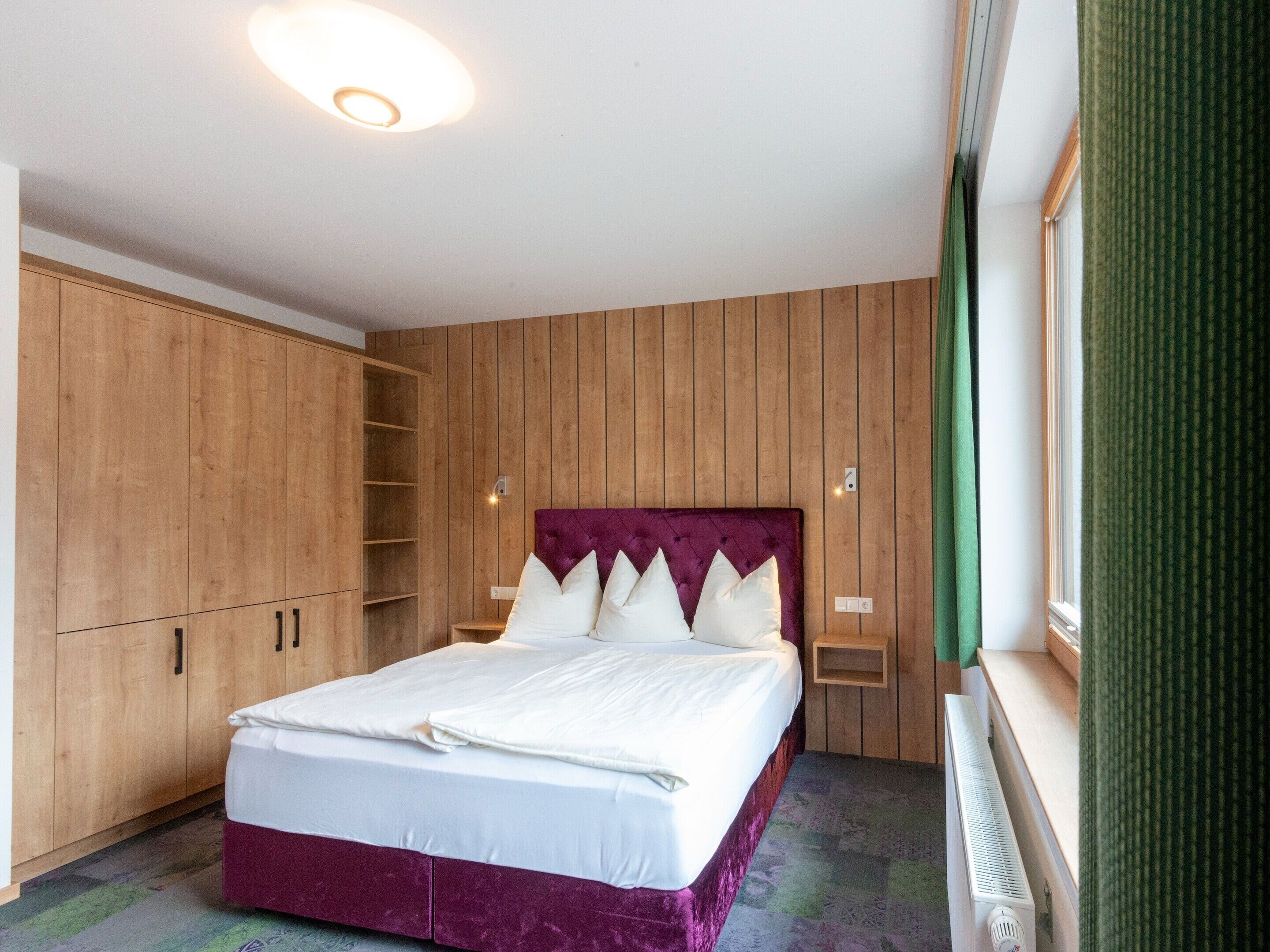 A bedroom with a bed, wooden wardrobe, and a window.