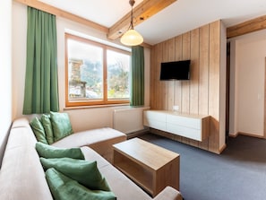 Een moderne woonkamer met een bank, een salontafel, een tv bevestigd aan een houten wand, en een uitzicht op bergen door grote ramen.