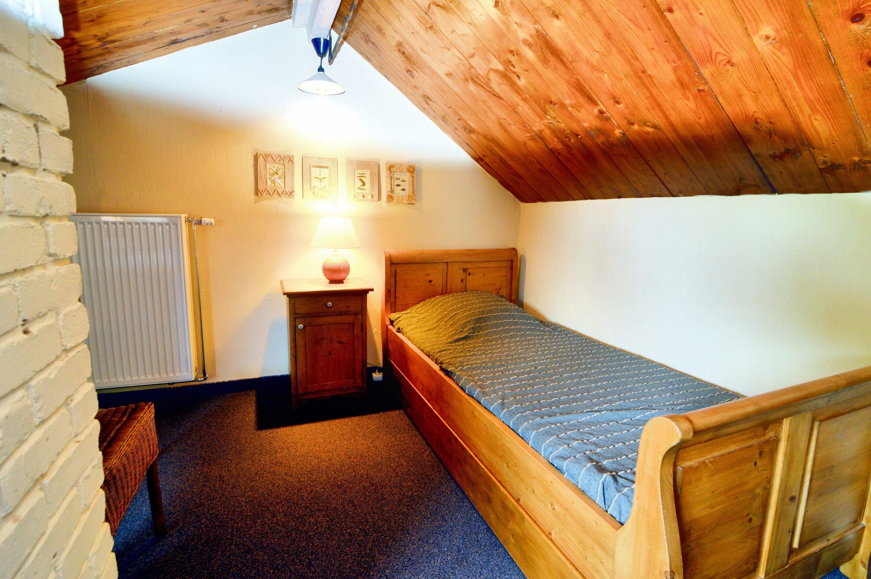 A small, cozy bedroom with a wooden bed, a nightstand, a lamp, and a radiator.
