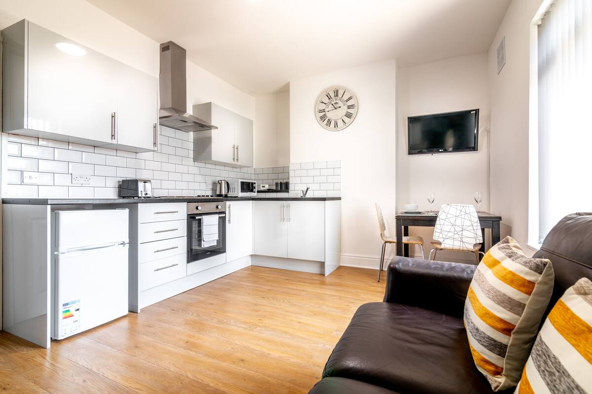 A modern kitchen with white cabinets, a built-in oven, and a large clock on the wall.