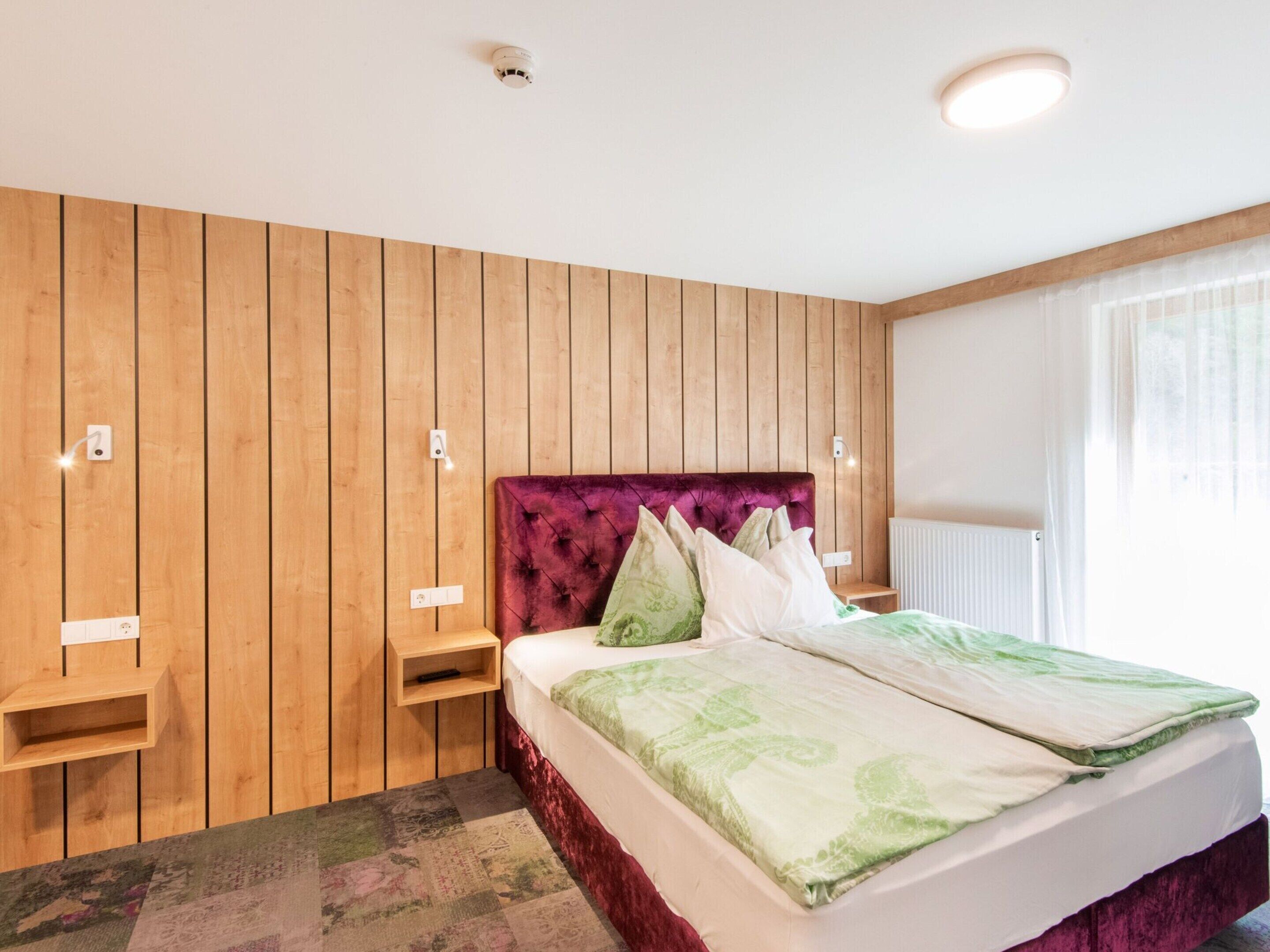 A hotel room with a wooden paneled wall, a bed with a green and white bedspread, and a red headboard.
