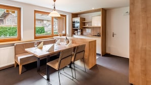 Cocina moderna con armarios de madera, una mesa de comedor con sillas y vistas al exterior a través de amplios ventanales.
