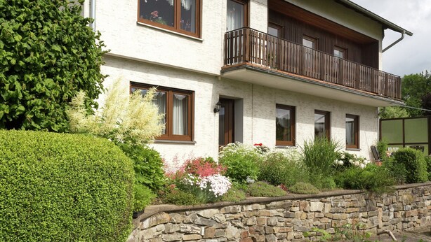 A two-story house with a stone wall and a paved driveway. - Ferienwohnung im Sauerland Hillside (Hallenberg)