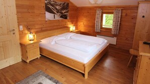A wooden cabin bedroom with a bed, nightstands, a window with curtains, a wall-mounted picture, and a ceiling light fixture. - Modern Chalet with Hot Tub in Krimml (Krimml)