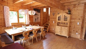 A wooden cabin with a dining area, wooden chairs, a table set for two, a staircase, and a cabinet with glass doors. - Modern Chalet with Hot Tub in Krimml (Krimml)