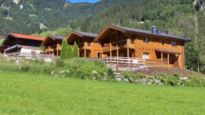 A wooden chalet with a balcony, set in a mountainous area with a clear sky. - Modern Chalet with Hot Tub in Krimml (Krimml)