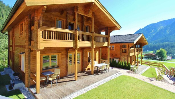 A two-story wooden cabin with a balcony, a deck with outdoor furniture, and a well-maintained lawn. - Modern Chalet with Hot Tub in Krimml (Krimml)